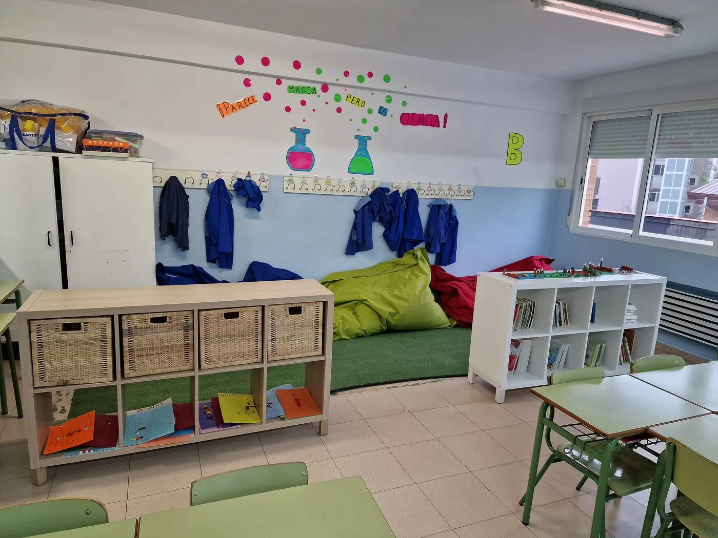 Rincón de un aula de Infantil con cojines verdes, cestas y estanterías