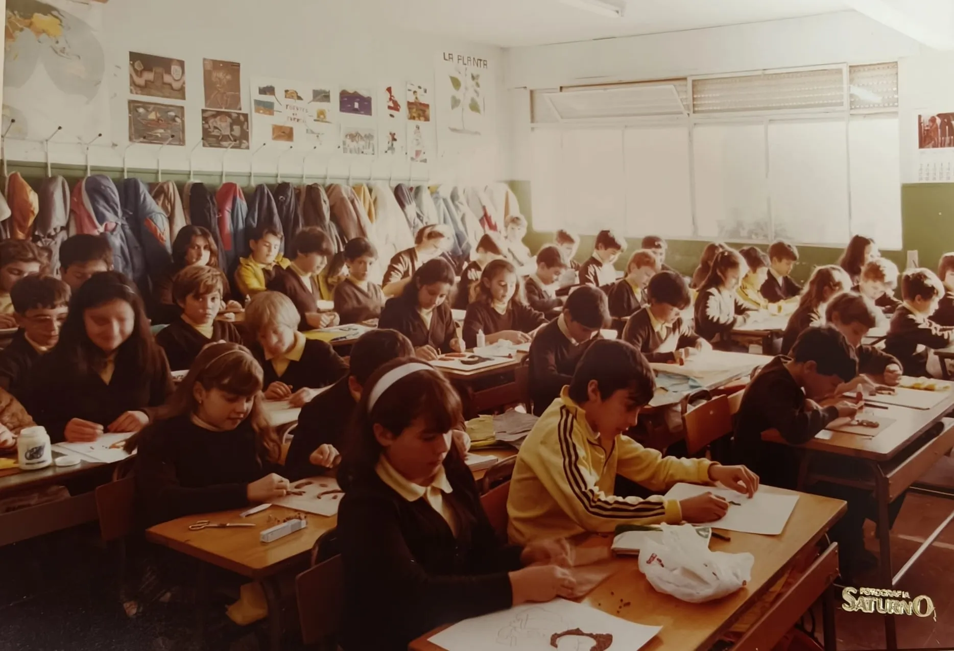 Alumnos trabajando en sus pupitres, con los abrigos colgados al fondo del aula